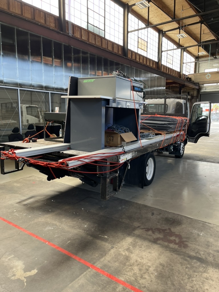 A flatbed truck in a shop, loaded with strapped aluminum profiles