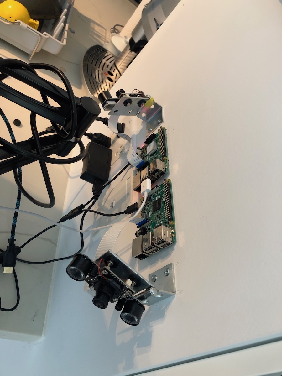 Two Raspberry Pi boards and a camera module mounted on a bracket, with cables running along a wall