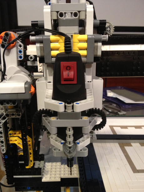 A hand dremel held in a Lego carriage, cutting a square groove into a block of green floral foam