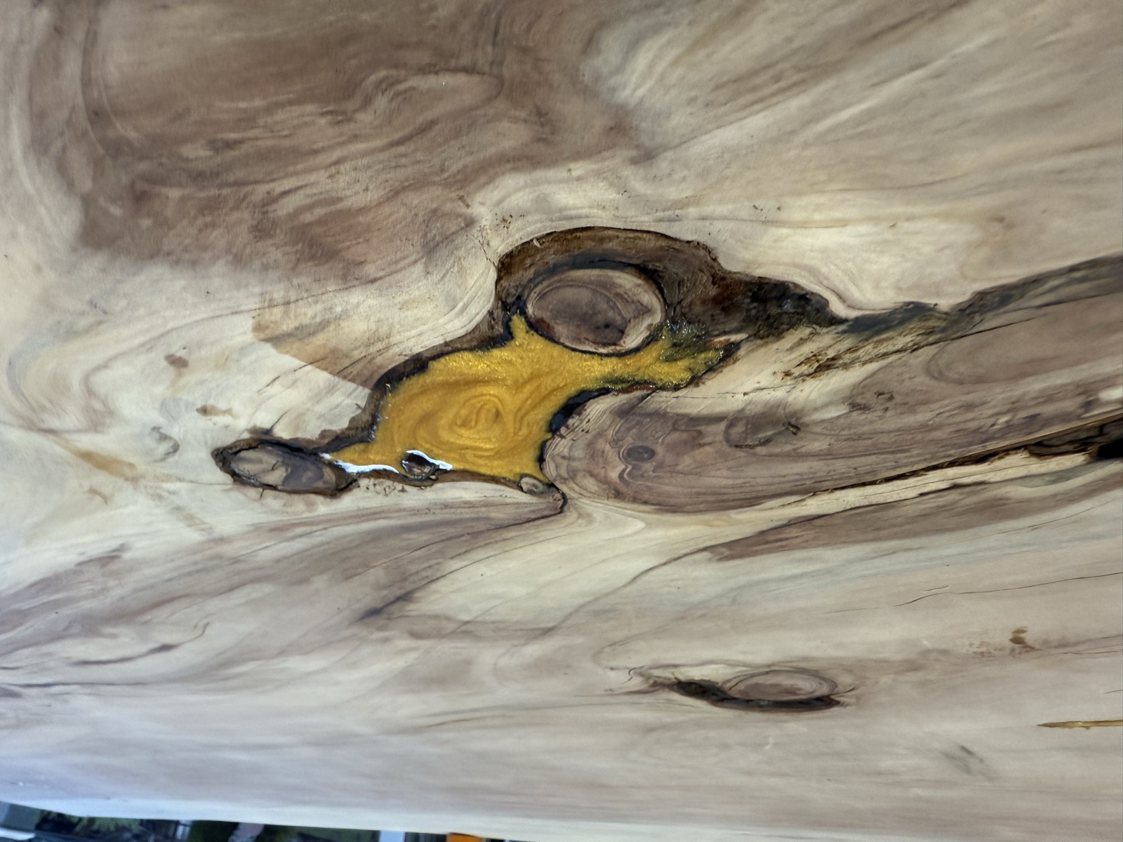 A knot hole filled with metallic gold epoxy, sanded flush with the surrounding grain