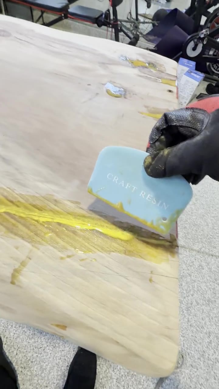 Spreading gold epoxy into a crack along the live edge with a plastic scraper