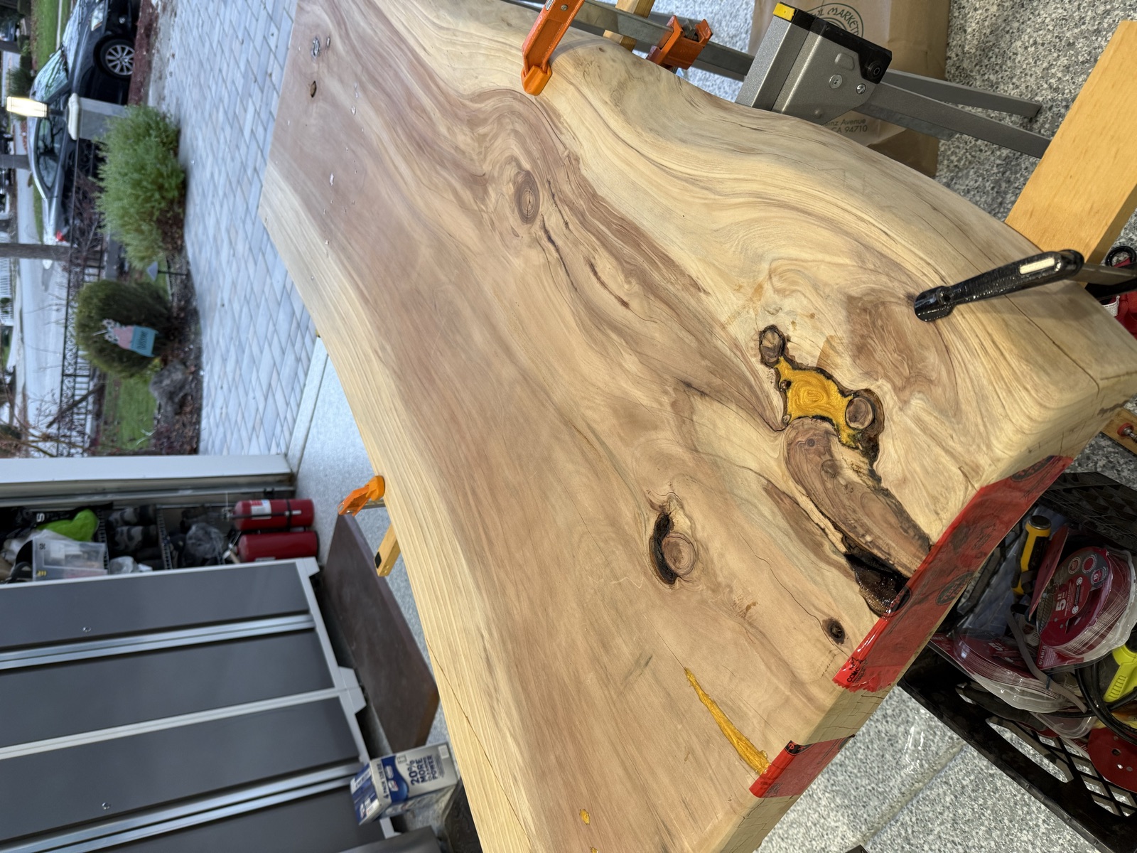The slab on sawhorses with bar clamps, red tape under a knot, and gold epoxy already in the hole