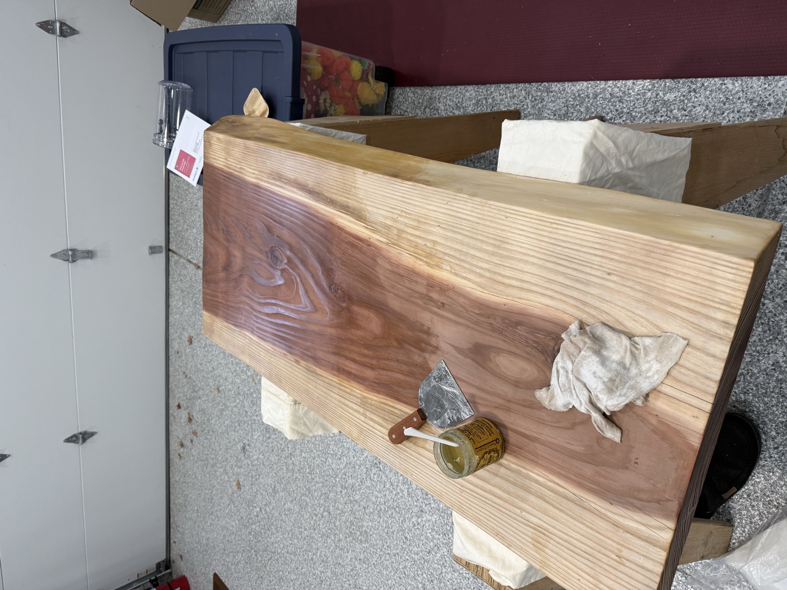 Oil jar, scraper, and rag on the slab, with the oiled heartwood dark and glossy