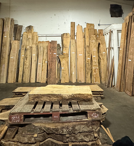 Live-edge slabs leaning against the wall at Peroba Reclaimed Wood, with a thick slab on a pallet in the foreground