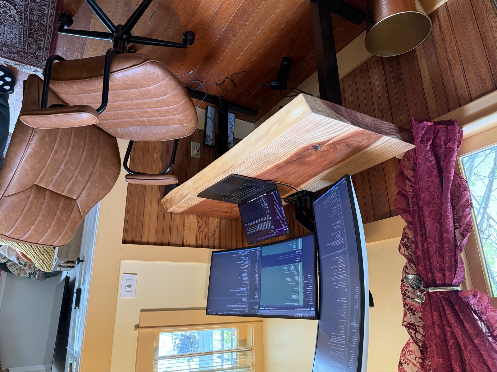 The finished redwood slab on a standing desk frame, with a laptop and two monitors