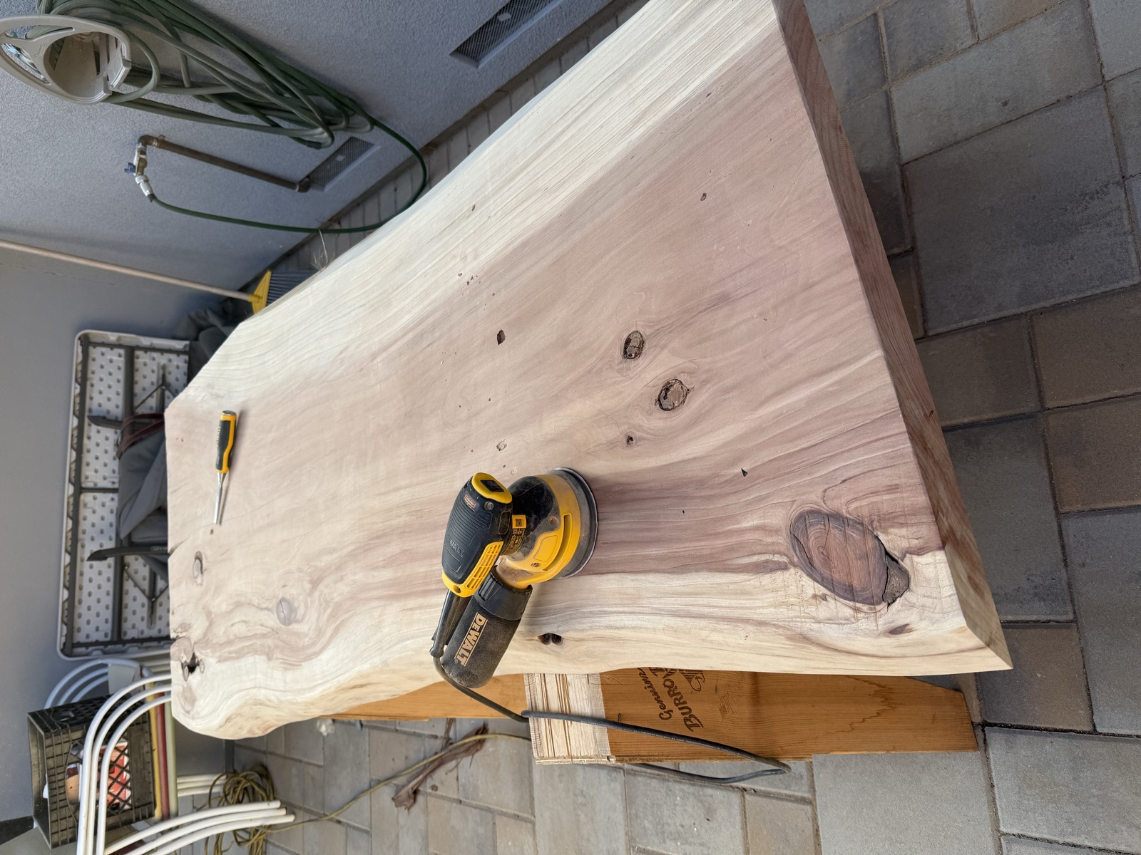 The second slab on sawhorses on the patio, with a DeWalt sander and a chisel on the surface