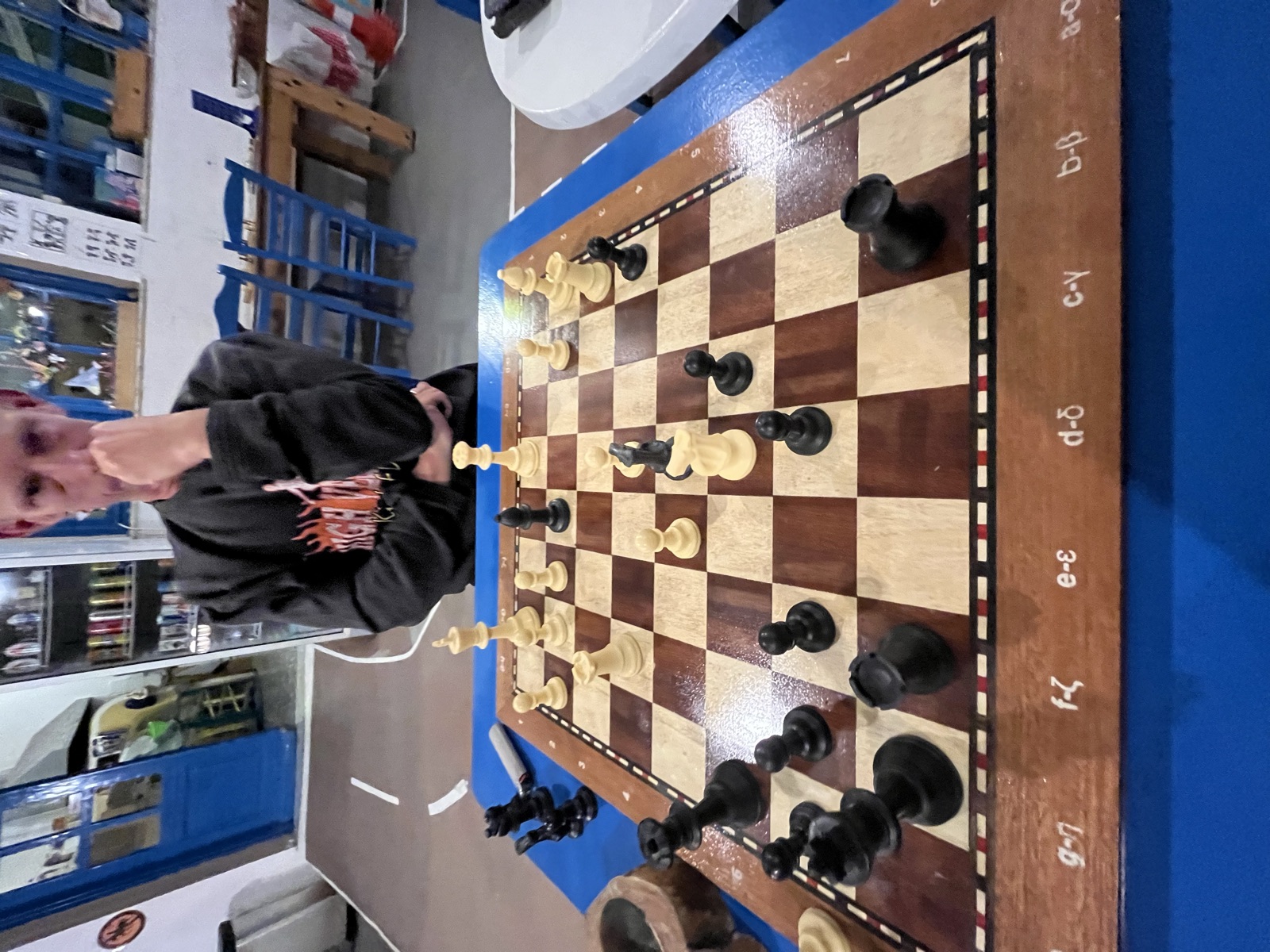 Playing chess at a blue table, the board labeled in Greek letters