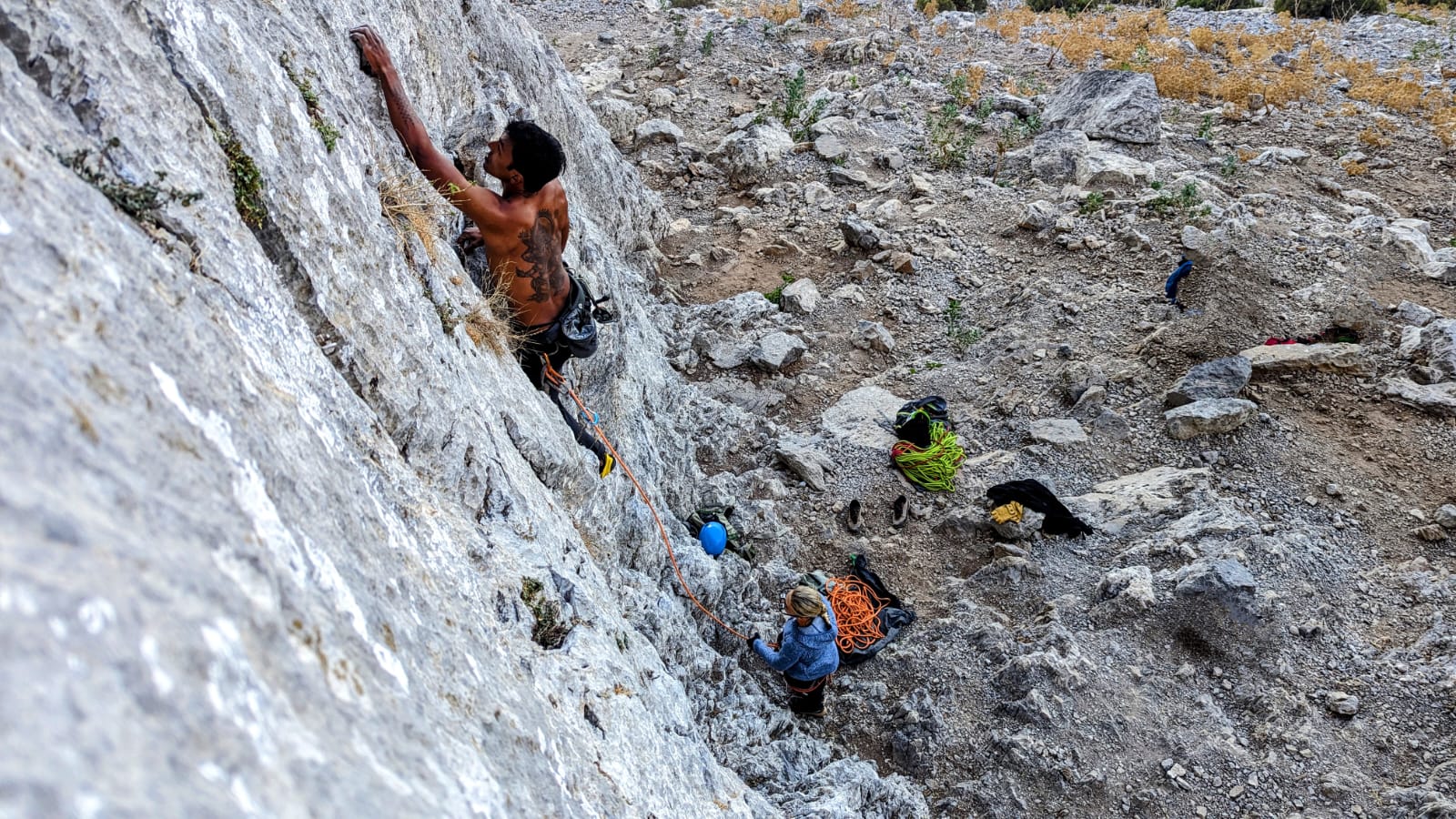 Leading a grey wall while a belayer watches from the scree