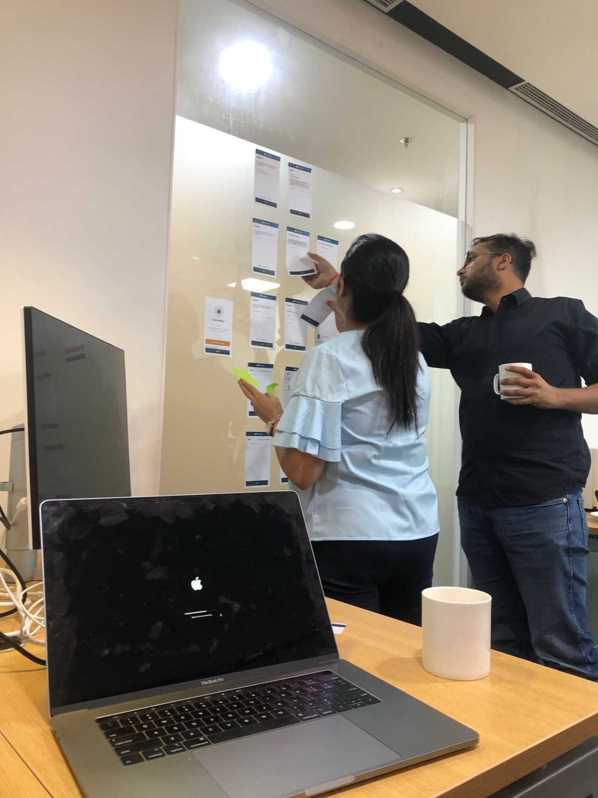 Two colleagues arranging printed app screens on a glass wall in the Delhi office